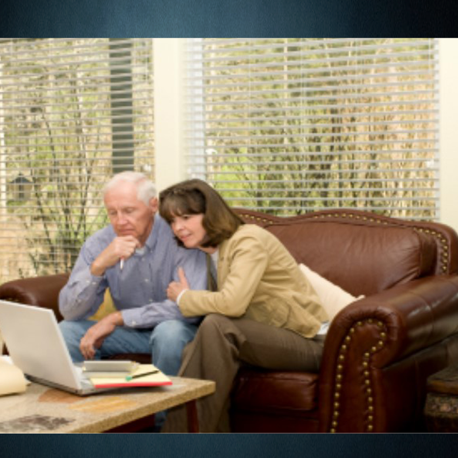A middle-aged couple sitting on their leather sofa are examining their finances on their laptop